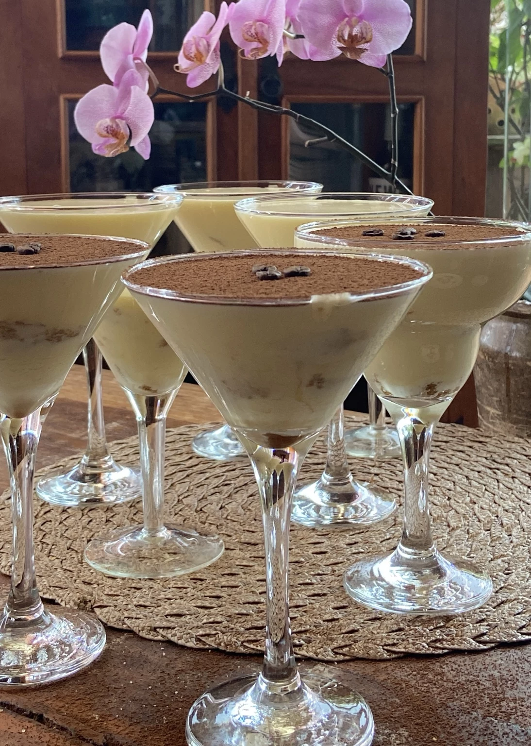 Taças de tiramisu com cacau, grãos de café e orquídeas ao fundo